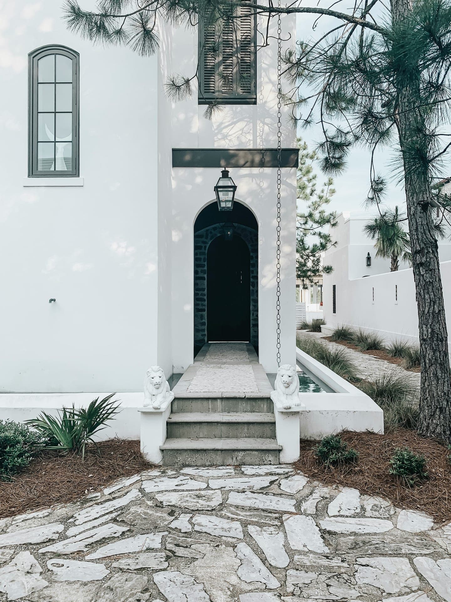 The white-stucco entry of an Alys Beach home along 30A — a stone path, arched doorway, and pines. The kind of property you can't simply drop by to check on.