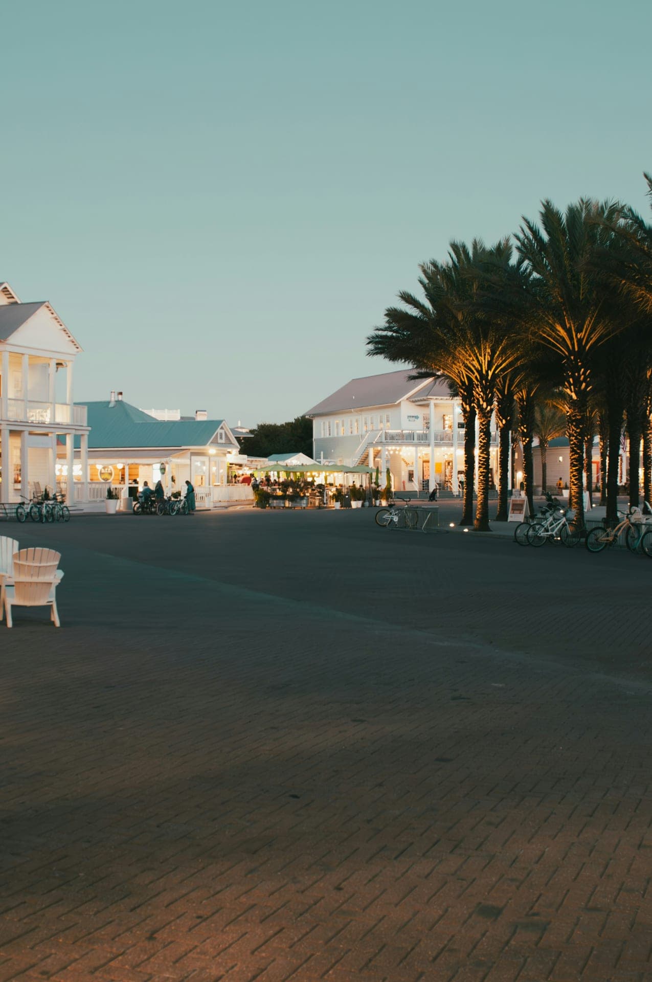 Seaside, Florida town center at dusk — palm trees, parked bicycles, and lit storefronts along the 30A corridor.